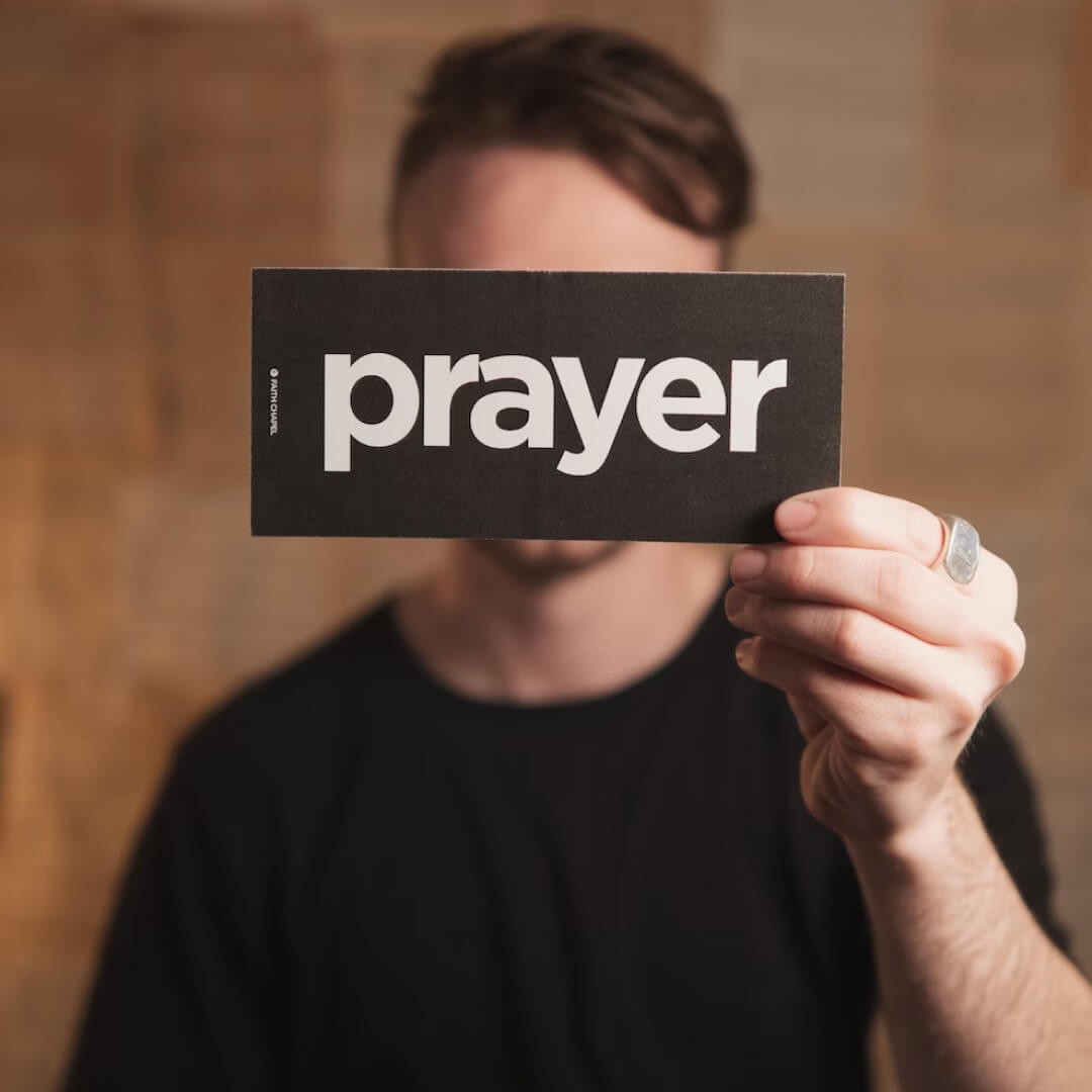 Person holding a card with the word “prayer” representing the importance of prayer in church life.