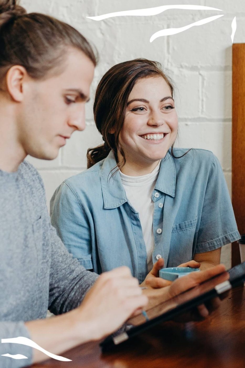 Two people sitting at a table looking at a tablet and talking.